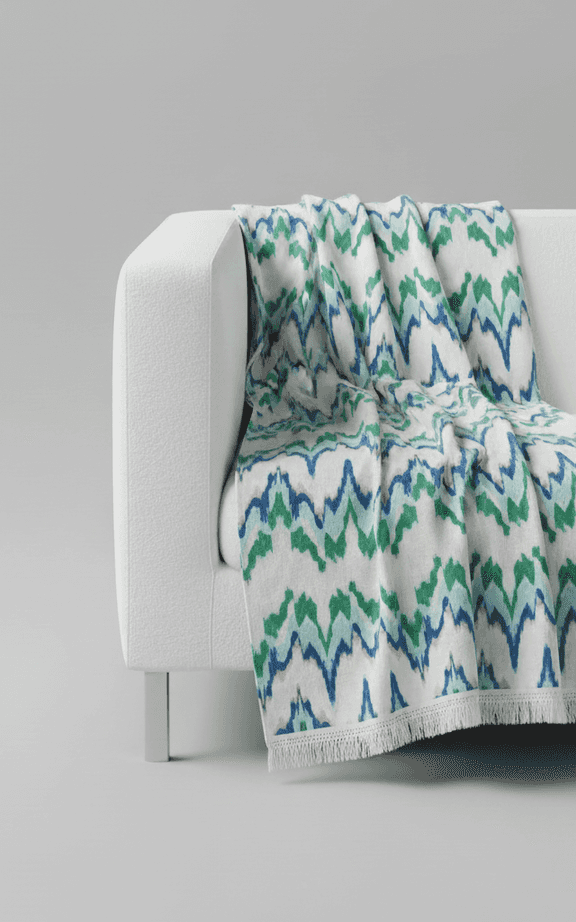 Manta de tamanho grande com padrão ikat azul e verde com borda de franjas sobre sofá branco